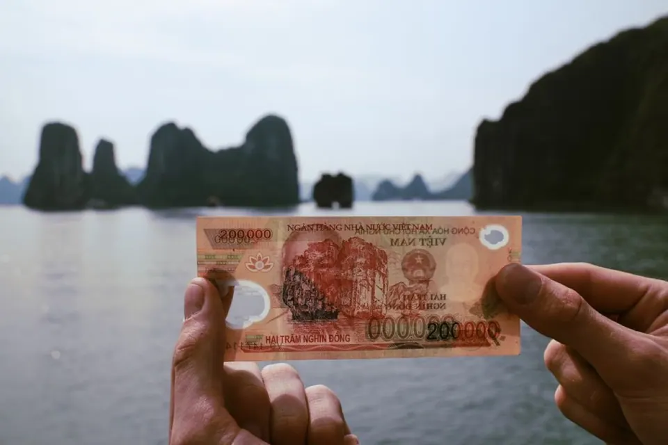 Người cầm tờ tiền Việt Nam trước vịnh biển